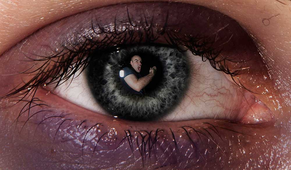 Farbfoto eines Auges, in dessen Pupille sich ein Mann spiegelt, der zum Schlag ausholt.