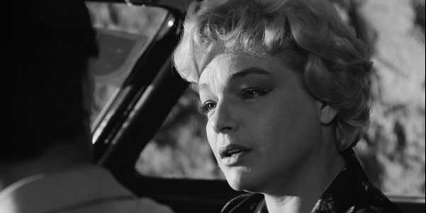 Schwarzweiß Foto für die-besten-spielfilme: Eine traurig aussehende Frau, die sich im Fond eines Wagens mit dem männlichen Fahrer unterhält.